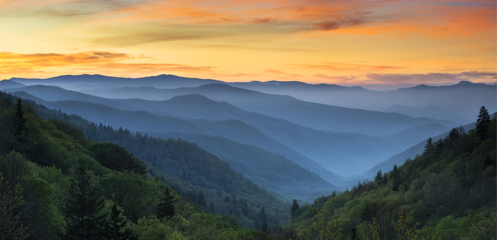 Sunset over layered mountain ridges with mist.